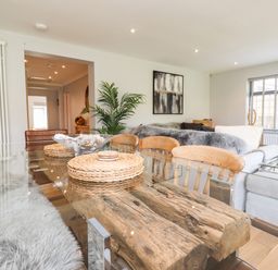 A dining area with a glass top wooden table surrounded by chairs next to a living room with a sofa and window blinds at Willow in Beadnell