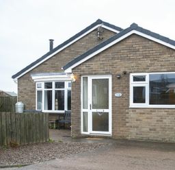 Front view of a brick bungalow with white framed windows and door a wooden fence and gravel driveway at Our Story Cottage in Longhoughton