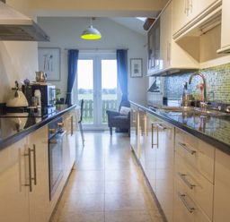 A kitchen with countertops cabinets a sink and a dining area with a chair and glass doors at Our Story Cottage in Longhoughton