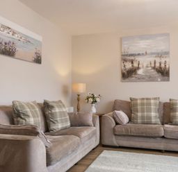 A living room with two beige sofas with plaid cushions a lamp and flower vase on a wooden table at Southfield Lodge in Seahouses