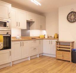 A kitchen with white cabinets wooden countertop microwave oven and clock on the wall at Southfield Lodge in Seahouses