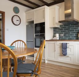 A kitchen with wooden dining table and chairs white cabinets and a stainless steel refrigerator at Kittiwake Cottage Seahouses