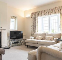 A living room with beige sofas floral curtains a television on a stand and a fireplace at Keepers View in Bamburgh