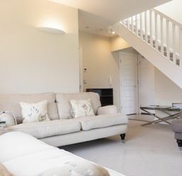 A living room with beige sofas and a glass coffee table under stairs at Keepers View in Bamburgh