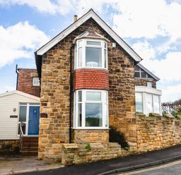 An exterior view of a stone house with bay windows and a blue door next to a stone wall on a street at The Beach House in Alnmouth