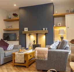 A living room with two gray sofas around a wooden coffee table and a dark blue fireplace at Wisteria Cottage in Warkworth