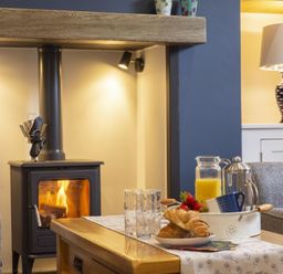 A living room with a wood stove fireplace and a coffee table with croissants orange juice and a coffee pot Wisteria Cottage in Warkworth