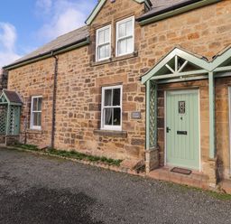 A stone cottage exterior with two green doors numbered 3 and 4 and windows at Willow Cottage in Lesbury