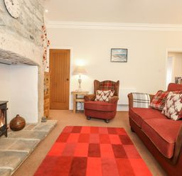 A living room with a wood burning stove a fireplace a red sofa and armchair with cushions a red checkered rug and a wooden door at Willow Cottage in Lesbury