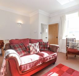 A living room with a red sofa and matching armchair near a window with curtains at Willow Cottage in Lesbury