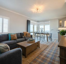A living room with a gray sofa an armchair a wooden coffee table and a dining table with chairs at Keildon in Seahouses