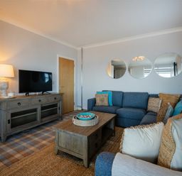 A living room with blue sectional sofa wooden coffee table and TV on wooden cabinet at Keildon in Seahouses