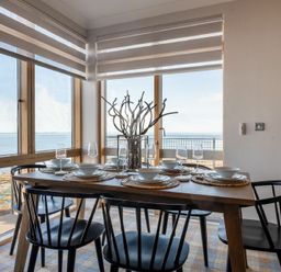 A dining area with a wooden table set for six with black chairs and a view of the sea at Keildon in Seahouses