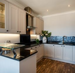 A kitchen with black countertops gray cabinets glass shelf and wooden floor at Keildon in Seahouses