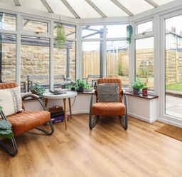 A conservatory with two brown chairs small white table and plants at Muscle Shoals in Seahouses