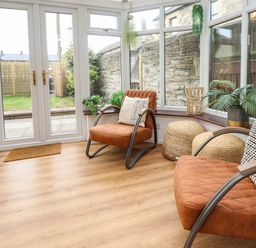 A conservatory with two orange chairs and plants by windows at Muscle Shoals in Seahouses