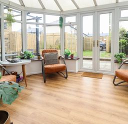 A conservatory with three armchairs a white round table hardwood flooring and plants at Muscle Shoals in Seahouses