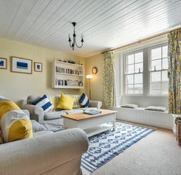 A living room with sofas, cushions, a coffee table, bookshelf, window seat, and patterned curtains at Sandpiper Cottage Low Newton-by-the-Sea