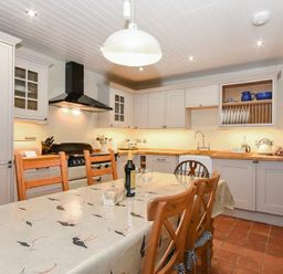 A kitchen with a wooden dining table and chairs a stove sink and cabinets at Sandpiper Cottage Low Newton-by-the-Sea