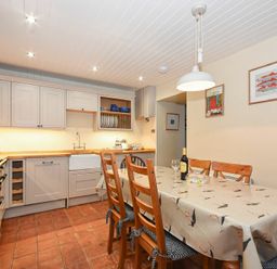 A kitchen with wooden cabinets dining table with six chairs a wine bottle and glass on table at Sandpiper Cottage Low Newton-by-the-Sea
