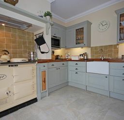 A kitchen with light gray cabinets wooden countertops a cream stove and a wall clock at Grange Cottage in Alnmouth