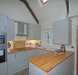 A kitchen with wooden countertops gray cabinets a stove a kettle and an oven at Martins Cottage in Alnmouth