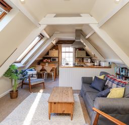 A living room with a gray sofa wooden coffee table and armchair facing a kitchen and dining area at Coach House (Alnmouth) in Alnmouth