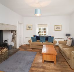 A living room with two beige sofas a wooden coffee table a gray rug and a stone fireplace at Avocet Cottage in Bamburgh