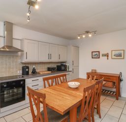 A kitchen with wooden dining table and chairs white cabinets and appliances at Avocet Cottage in Bamburgh