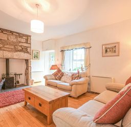 A living room with two sofas a wooden coffee table a stone fireplace and a window at Dunlin Cottage in Bamburgh