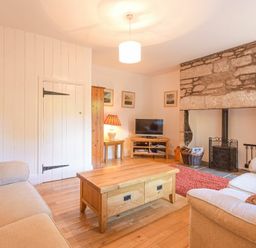 A living room with two sofas a wooden coffee table a stone fireplace a television and a lamp at Dunlin Cottage in Bamburgh