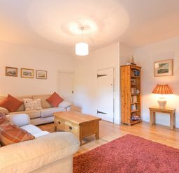 A living room with beige sofas wooden coffee table wooden bookshelf and red rug at Dunlin Cottage in Bamburgh