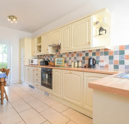 A kitchen with cream cabinets tiled backsplash oven and wooden dining table at Dunlin Cottage in Bamburgh