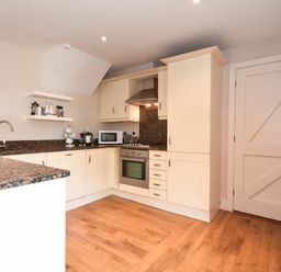 A kitchen with white cabinets a microwave an oven and a wooden floor at High Tide in Newton-by-the-Sea