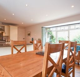 A dining area with wooden chairs and table next to a kitchen with an island and large windows at High Tide in Newton-by-the-Sea