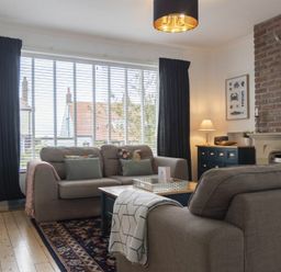 A living room with two sofas a coffee table a sideboard a lamp and a brick fireplace at Sea Croft in Beadnell