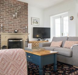 A living room with a brick fireplace a gray sofa a blue coffee table and a television at Sea Croft in Beadnell