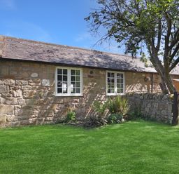 An outdoor view of a stone cottage with a garden at Plumtree Cottage in Alnmouth