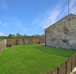 A garden with grass, a chair, and flower pots at Plumtree Cottage in Alnmouth
