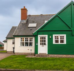 A house with white walls and a green wooden extension with windows and a door at Armstrong Cottages No30 in Bamburgh