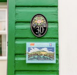 Green wooden wall with house number 30 and a northumbria cottages sign at Armstrong Cottages No30 in Bamburgh