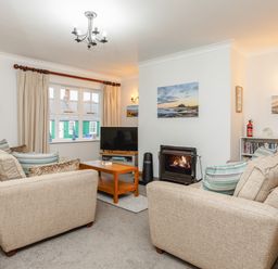 A living room with two beige sofas a wooden coffee table a fireplace and a television at Armstrong Cottages No30 in Bamburgh