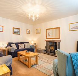A living room with sofas a coffee table a fireplace and framed pictures on the walls at Lobster Pot Cottage in Seahouses