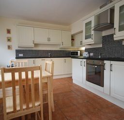 A kitchen with wooden dining table and chairs and white cabinets at Lobster Pot Cottage in Seahouses