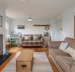 A living room with two checkered sofas a wooden chest coffee table a desk with chair and a fireplace at Beachward in Embleton