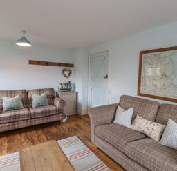 A living room with two plaid sofas wooden floor and a framed map on the wall at Beachward in Embleton