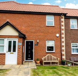 A brick house exterior with two doors wooden bench and garden at The Apartment in Bamburgh