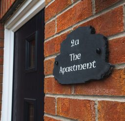 A black door with white frame and a black sign with white text on a brick wall at The Apartment in Bamburgh