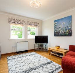 A living room with a red sofa brown sofa a television on a glass stand a wooden coffee table and a floral painting on the wall at The Apartment in Bamburgh