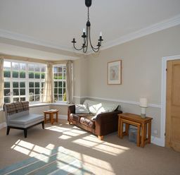 A living room with a brown sofa a small chair wooden side tables a lamp a TV and large windows at Beach House (Alnmouth) in Alnmouth